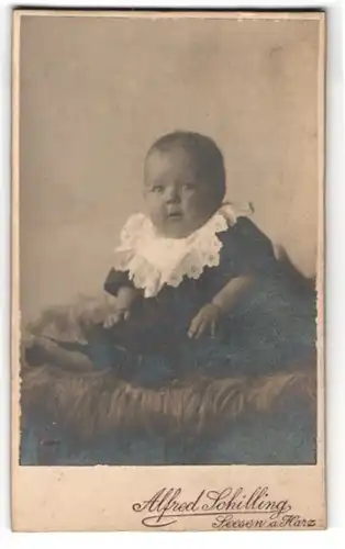 Fotografie Alfred Schiling, Seesen a. Harz, Portrait niedliches Baby im gestreiften Kleid auf Fell sitzend