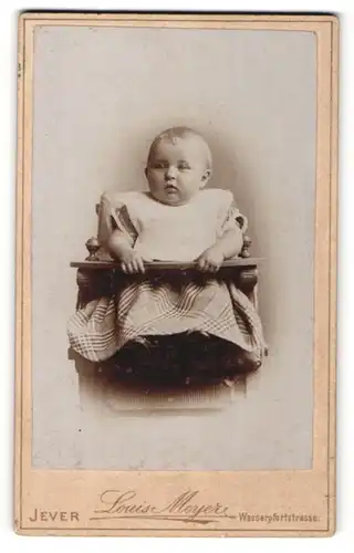 Fotografie Louis Meyer, Jever, Portrait niedliches Baby im karierten Kleid mit Latz im Hochstuhl