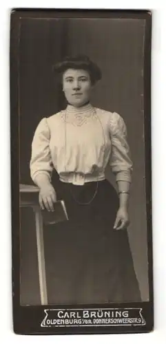 Fotografie Carl Brüning, Oldenburg i / Gr., Portrait junge lächelnde Dame in weisser Bluse mit Buch an Tisch gelehnt