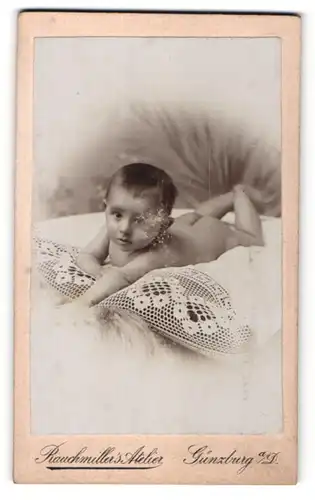 Fotografie Raumiller`s Atelier, Günzburg a / D., Portrait Kleinkind auf einem Kissen liegend