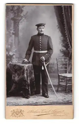 Fotografie Atelier Carl Beste, Minden i / W., Portrait Soldat in Uniform mit Schirmmütze und Degen an Tisch gelehnt