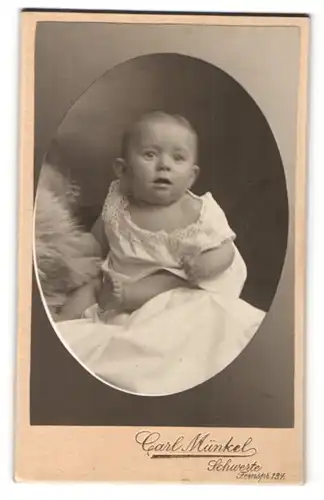 Fotografie Carl Münkel, Schwerte, Portrait niedliches Baby im weissen Hemd mit Fell auf Laken sitzend