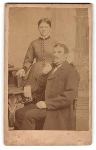 Fotografie Carl Wolf, Celle, Portrait älterer Mann mit Oberlippenbart u. Fliege auf Stuhl sitzend mit Frau
