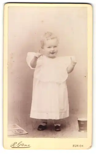 Fotografie R. Ganz, Zürich, Portrait kleines lächelndes Mädchen im weissen Kleid