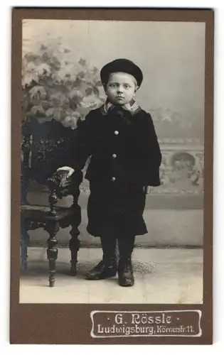 Fotografie G. Rössle, Ludwigsburg, Portrait kleiner Junge mit Hut im Anzug an Stuhl gelehnt