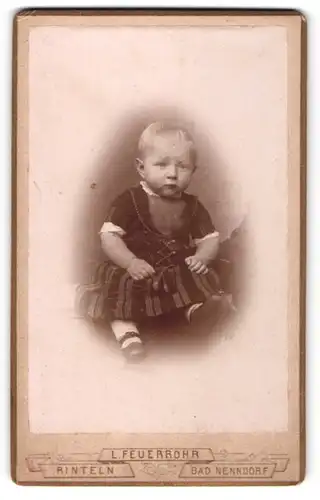 Fotografie L. Feuerrohr, Rinteln, Bad Nenndorf, Portrait niedliches Kleinkind im gemusterten Kleid auf Tisch sitzend