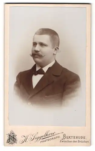 Fotografie H. Siggelkow, Buxtehude, Portrait bürgerlicher Herr mit Zwirbelbart u. Fliege im Anzug