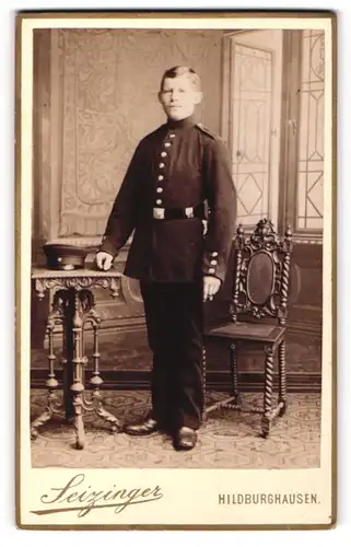 Fotografie Seizinger, Hildburghausen, Portrait Soldat in Uniform mit Schirmmütze an Tisch gelehnt