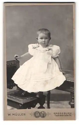 Fotografie W. Müller, Magdeburg, Portrait kleines Mädchen im weissen Kleid auf Tisch sitzend