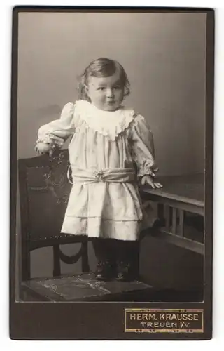 Fotografie Herm. Krausse, Treuen i / V., Portrait niedliches kleines Mädchen im hübschen Kleid auf Stuhl stehend