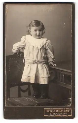 Fotografie Herm. Krausse, Treuen i / V., Portrait niedliches kleines Mädchen im hübschen Kleid auf Stuhl stehend