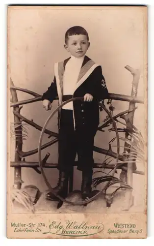 Fotografie Edg. Wallnau, Berlin N., Portrait kleiner Junge im Matrosenanzug mit Reifen an Geländer gelehnt