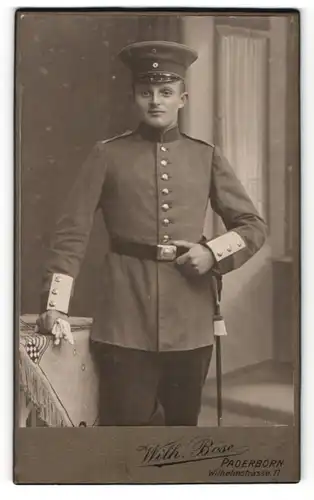 Fotografie Wilh. Böse, Paderborn, junger Soldat mit Mütze und Hand an Gürtel