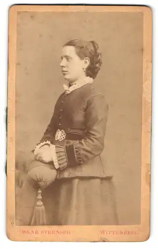 Fotografie Oskar Strensch, Wittenberg, Portrait lächelnde Dame mit Flechtfrisur in eleganter Kleidung an Sessel gelehnt