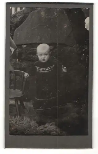 Fotografie W. Lüdecke, Hannover, Portrait niedliches Kleinkind im hübschen Kleid an Stuhl gelehnt