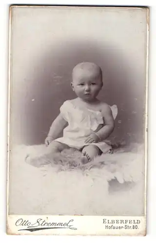 Fotografie Otto Stremmel, Elberfeld, Portrait niedliches Baby im weissen Hemd auf Fell sitzend