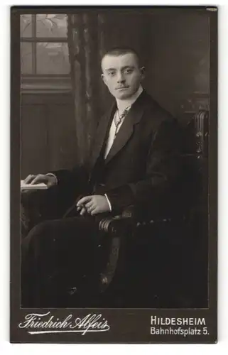 Fotografie Friedrich Alfeis, Hildesheim, Portrait junger Herr mit Oberlippenbart u. Zigarre im Anzug auf Stuhl sitzend
