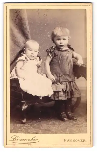 Fotografie G. W. Leineweber, Hannover, Portrait niedliches Baby auf Stuhl sitzend u. Kleinkind an Tisch gelehnt