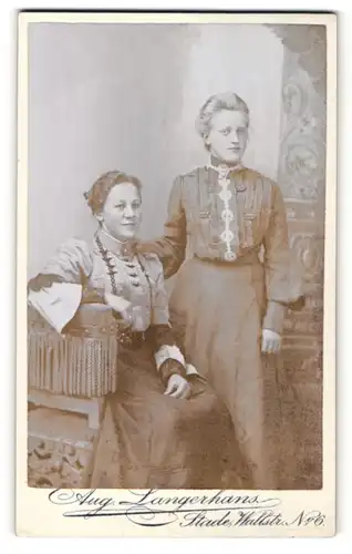 Fotografie Aug. Langerhans, Stade, Portrait lächelnde Dame mit zurückgebundenem Haar auf Hocker sitzend mit junger Dame