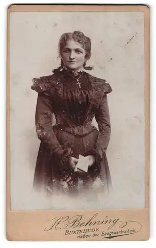 Fotografie H. Behning, Buxtehude, Portrait junge Dame mit Kreuzkette u. Buch im eleganten Kleid