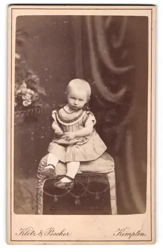 Fotografie Klotz & Bscher, Kempten, Portrait niedliches Kleinkind im hübschen Kleid auf Hocker sitzend