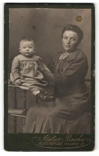 Fotografie Atelier Becke, Bleicherode, Portrait lächelnde Mutter mit zurückgebundenem Haar auf Hocker sitzend mit Baby