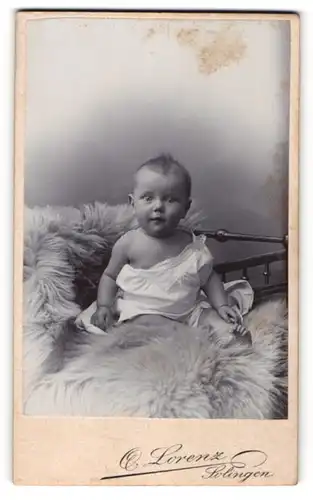 Fotografie Otto Lorenz, Solingen, Portrait niedliches Baby im weissen Hemd auf Fell sitzend