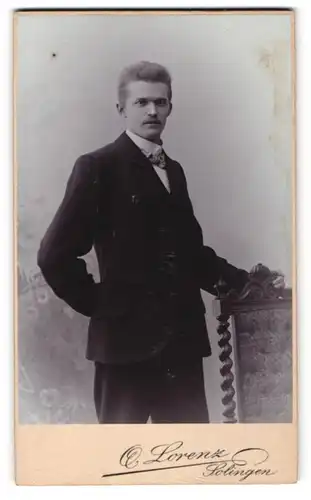 Fotografie Otto Lorenz, Solingen, Portrait junger Herr mit Oberlippenbart u. Fliege im Anzug an Stuhl gelehnt