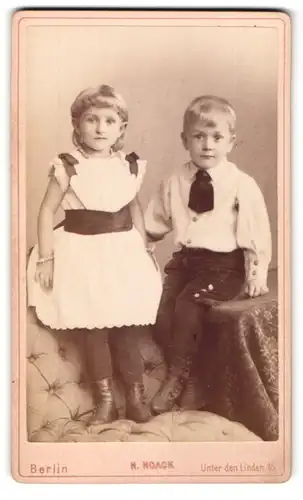 Fotografie H. Noack, Berlin, Portrait kleines Mädchen im hübschen Kleid auf Sessel stehend u. Junge auf Tisch sitzend
