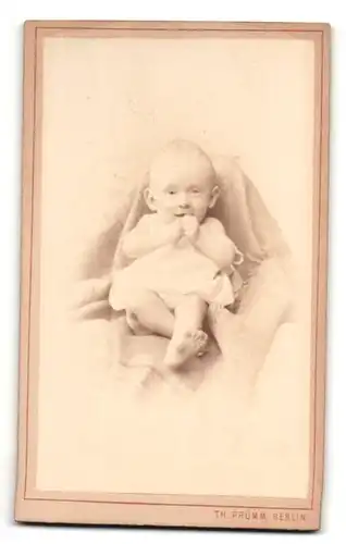 Fotografie Th. Prümm, Berlin, Portrait niedliches Baby im weissen Hemd auf Decke sitzend