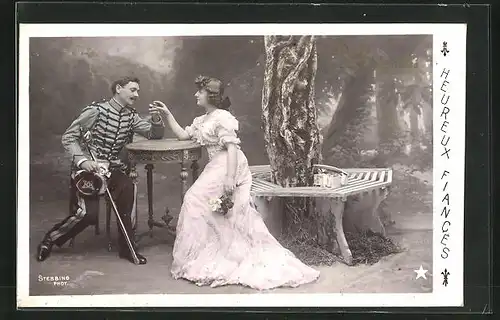 Foto-AK Stebbing: La Bague de Fiancailles, Herr in Uniform und Dame sitzen am Tisch unter einem Baum