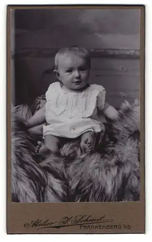 Fotografie Atelier J. Schmit, Frankenberg i / S., Portrait niedliches Kleinkind im weissen Hemd auf Fell sitzend