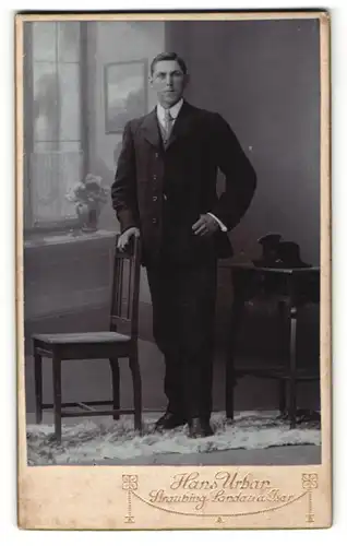 Fotografie Hans Urban, Straubing, Portrait charmanter Herr mit Seitenscheitel u. Krawatte im Anzug an Stuhl gelehnt