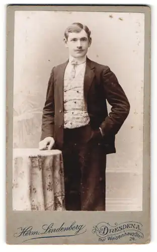 Fotografie Herm. Lindenberg, Dresden-A., Portrait junger Herr mit Krawatte im Anzug an Tisch gelehnt