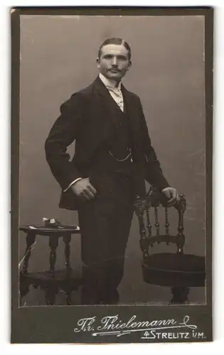 Fotografie Th. Thielemann, Strelitz i / M., Portrait charmanter Herr mit Krawatte im Anzug an Stuhl gelehnt