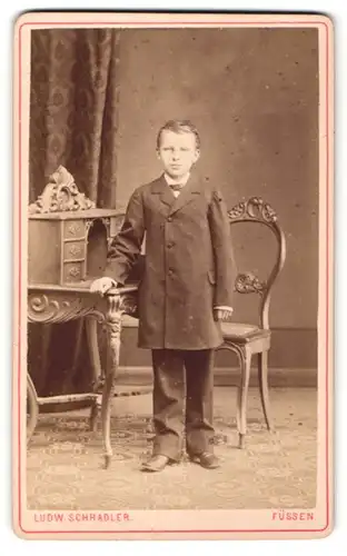 Fotografie Ludw. Schradler, Füssen, Portrait kleiner Junge in zeitgenöss. Kleidung an Tisch gelehnt