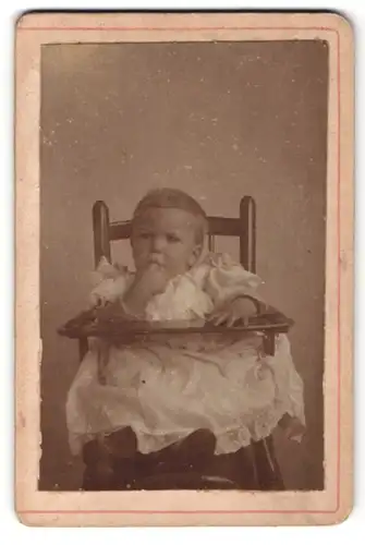 Fotografie Fotograf unbekannt, Ort unbekannt, kleines Mädchen in Spitzenkleid im Hochstuhl sitzend