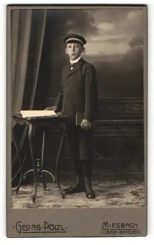 Fotografie Georg Pöltl, Miesbach, Junge in Anzug mit kurzen Hosen mit Mütze und Buch haltend