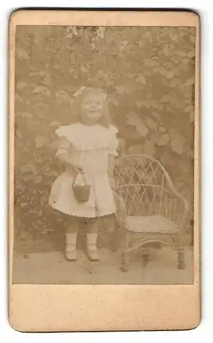 Fotografie Fotograf unbekannt, Ort unbekannt, kleines Mädchen in Rüschenkleid mit Eimerchen und lachend