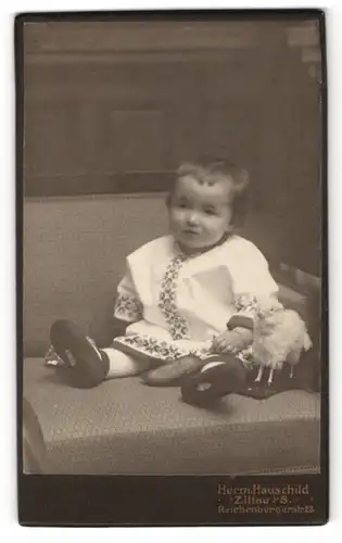 Fotografie Herm. Hauschild, Zittau, kleines Mädchen in besticktem Kleid mit Schaf Spielzeug