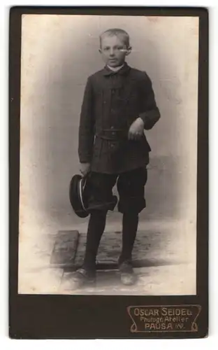 Fotografie Oscar Seidel, Pausa i. V., Junge mit kurzen Hosen und Mütze in Hand haltend