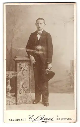 Fotografie Carl Steinert, Helmstedt, Junge in Dreiteiler mit Fliege und Mütze in Hand