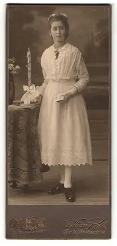 Fotografie William Roth, Berlin S. O., Portrait junge Dame im weissen Kleid mit Buch u. Kerze an Tisch glehnt