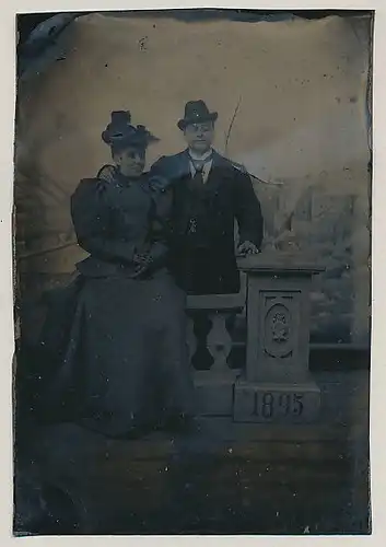Fotografie Ferrotypie elegantes Paar im feinen Zwirn mit Hut, Säule mit Wappen und Jahreszahl 1895