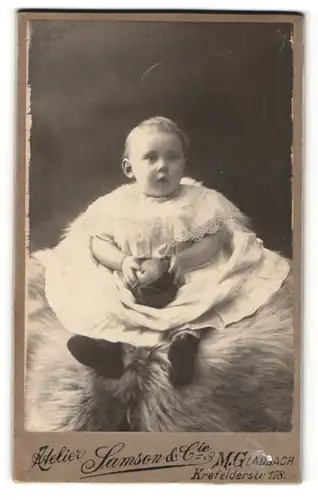 Fotografie Atelier Samson & Cie, M. Gladbach, Portrait niedliches Kleinkind im hübschen Kleid mit Ball auf Fell sitzend