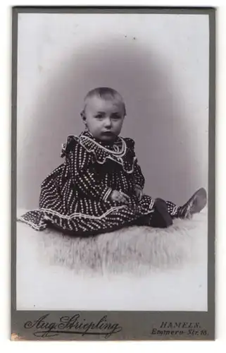 Fotografie Aug. Striepling, Hameln, Portrait niedliches Kleinkind im hübschen Kleid auf Fell sitzend