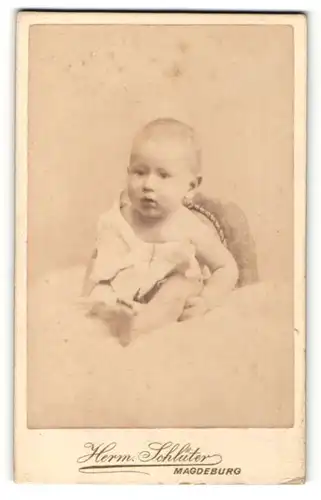 Fotografie Herm. Schlüter, Magdeburg, Portrait niedliches Kleinkind im weissen Hemd auf Fell sitzend