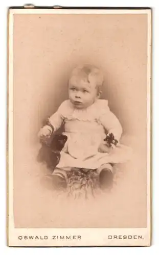 Fotografie Oswald Zimmer, Dresden, Portrait niedliches Baby im weissen Kleid auf Fell sitzend