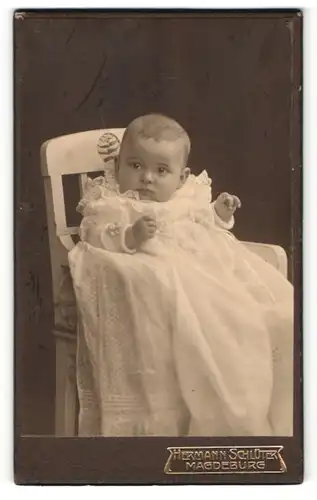 Fotografie Hermann Schlüter, Magdeburg, Portrait niedliches Baby im weissen Kleid auf Hochstuhl sitzend