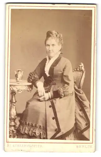 Fotografie J. C. Schaarwächter, Berlin, Portrait lächelnde Dame mit Hochsteckfrisur am Tisch sitzend